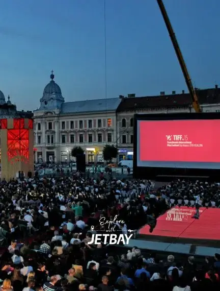Evening crowd gathered at outdoor film festival in Cluj-Napoca's historic city center with baroque architecture