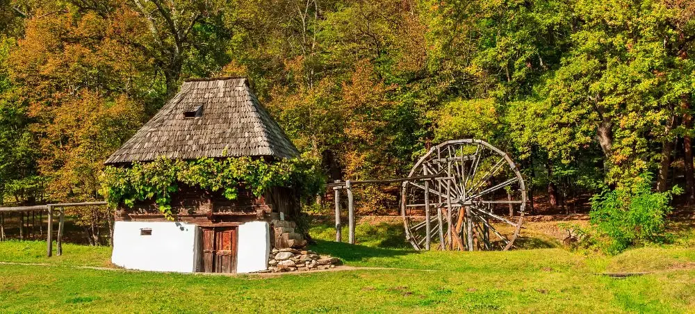 Traditional Romanian countryside cottage with thatched roof and wooden waterwheel in autumn forest near Cluj-Napoca