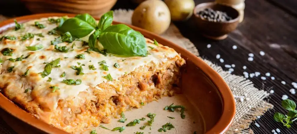 Traditional Romanian lasagna with fresh basil and herbs served in terracotta dish, showcasing Cluj-Napoca cuisine