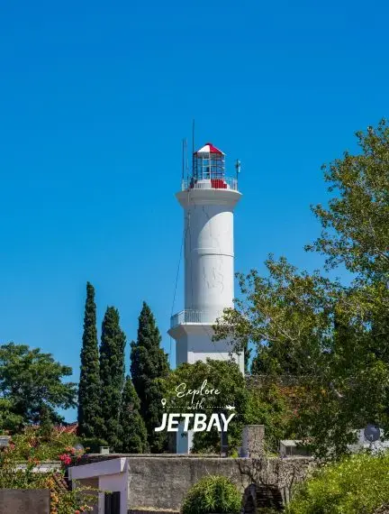 Historic white lighthouse tower surrounded by lush greenery under clear blue sky in Colonia del Sacramento