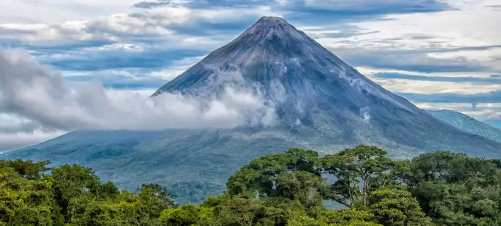 Majestic Arenal Volcano rising through misty clouds above Costa Rica's lush rainforest canopy