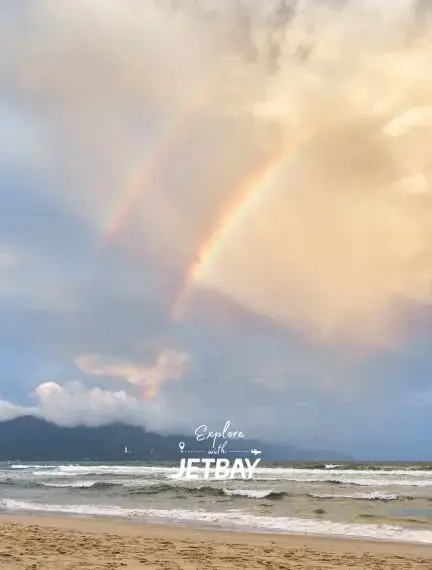 Double rainbow arcs over pristine Da Nang beach with golden sand and rolling waves under dramatic sky