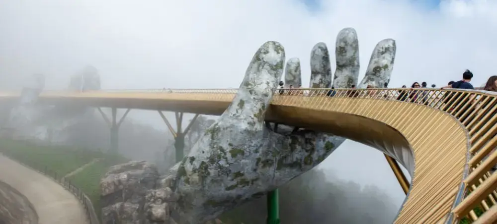 Golden Bridge in Da Nang held by giant stone hands with tourists walking across misty mountain landscape