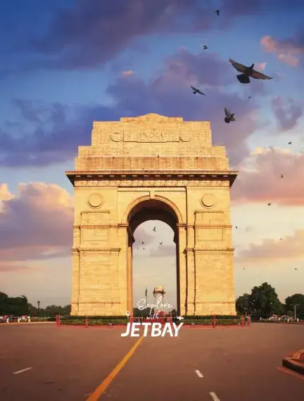 India Gate war memorial illuminated at golden hour with birds flying overhead in Delhi's evening sky