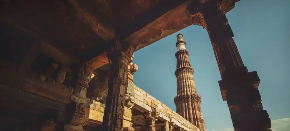 Qutub Minar tower viewed through ancient stone arches in Delhi, showcasing India's historic architecture