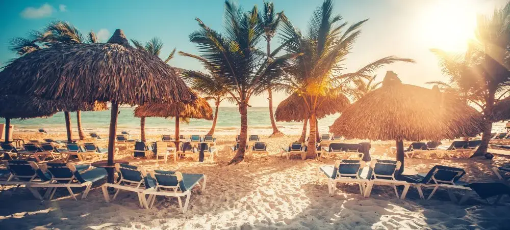 Pristine Dominican Republic beach resort with palm trees, thatched umbrellas and lounge chairs at golden sunset