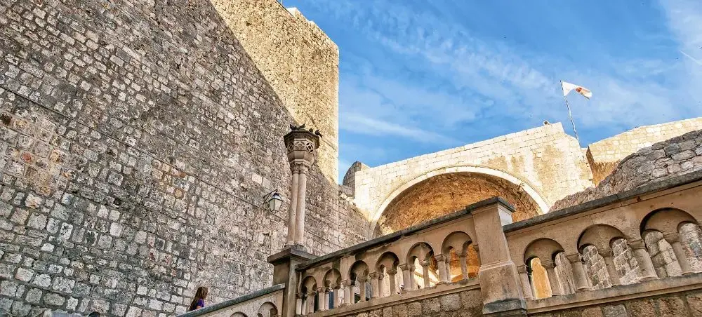 Medieval stone walls and arched colonnade of Dubrovnik's Old Town fortress under bright blue sky