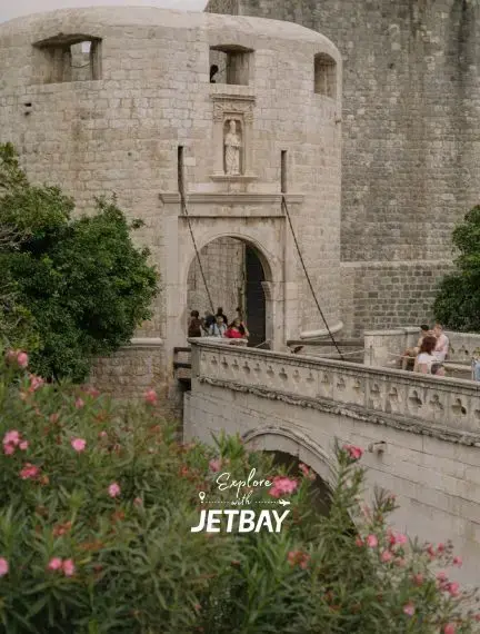 Historic stone bridge leading to medieval fortress gate in Dubrovnik's Old Town with tourists exploring