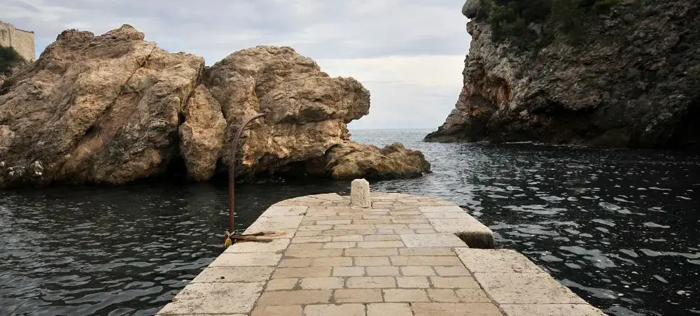 Stone pier extending into azure waters surrounded by dramatic limestone cliffs in Dubrovnik's coastline