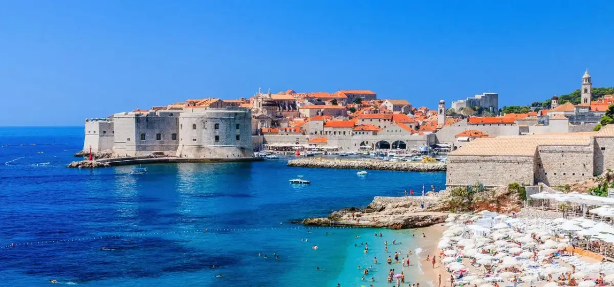 Dubrovnik's historic walled city and azure harbor with beachgoers enjoying crystal-clear Adriatic waters