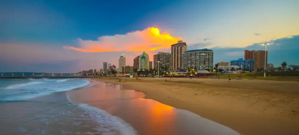 Durban beachfront skyline at sunset with golden sand beach and luxury hotels reflecting in ocean waves