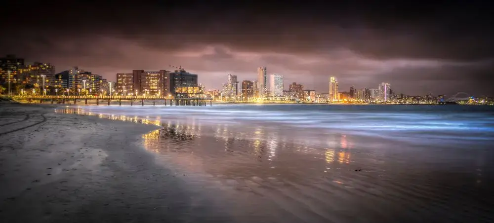 Durban's illuminated beachfront skyline reflecting on wet sand during twilight, showcasing South Africa's coastal city