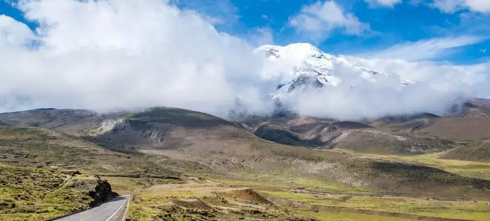 Scenic highway leading through Ecuador's Andean highlands toward snow-capped Chimborazo volcano under dramatic clouds