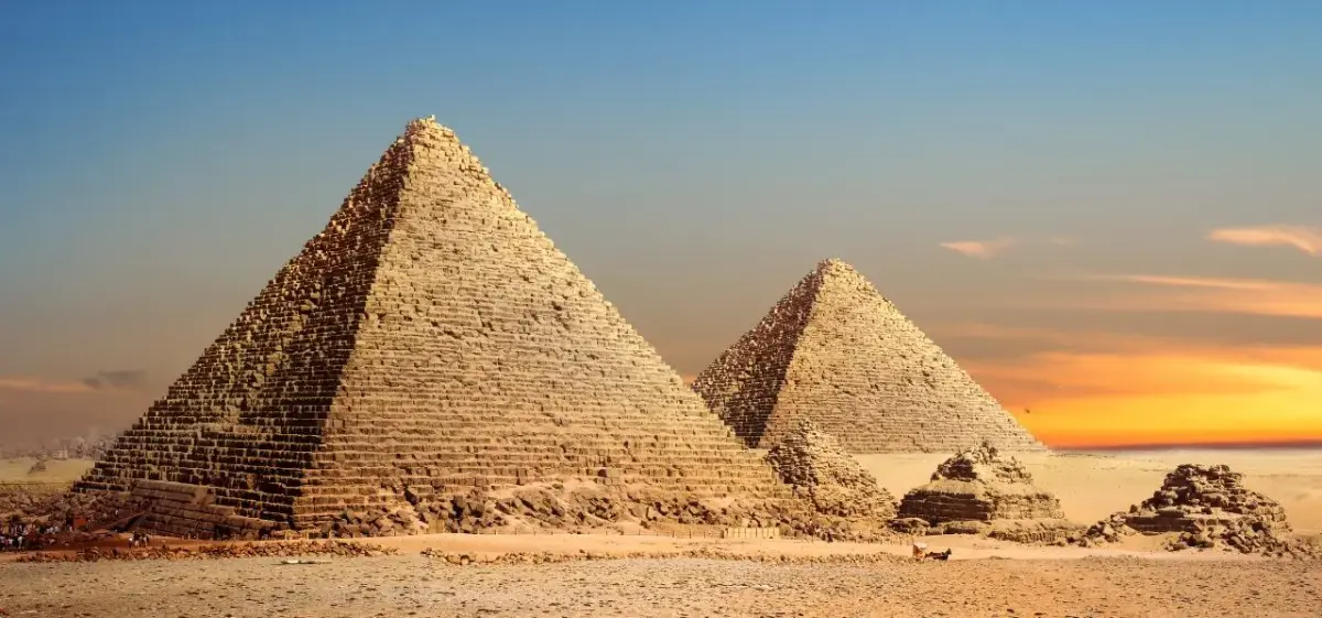 Ancient pyramids of Giza rising majestically from golden desert sands under dramatic sunset sky in Egypt