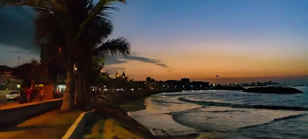 Tropical beachfront promenade at sunset in El Salvador with palm trees and gentle waves along the coastline