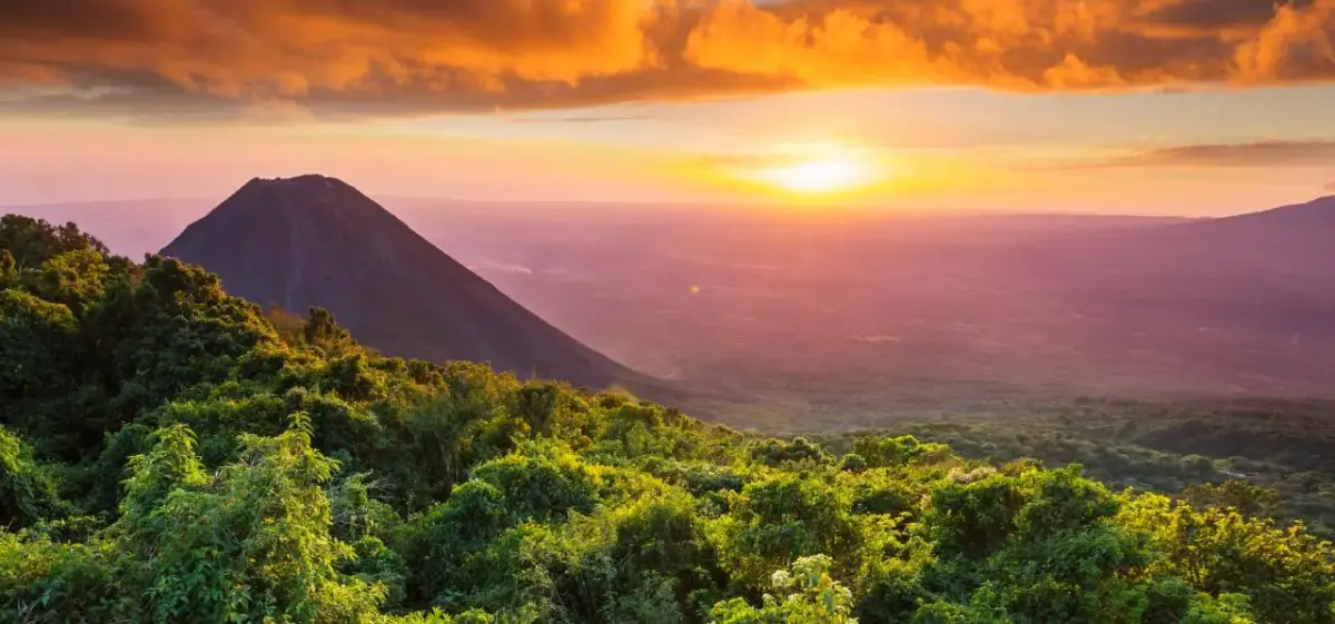 Dramatic sunset over volcanic peak and lush rainforest canopy in El Salvador's mountainous landscape