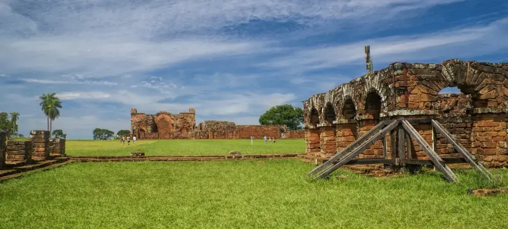 Ancient stone ruins of Jesuit missions in Encarnacion Paraguay with green grass and blue sky backdrop