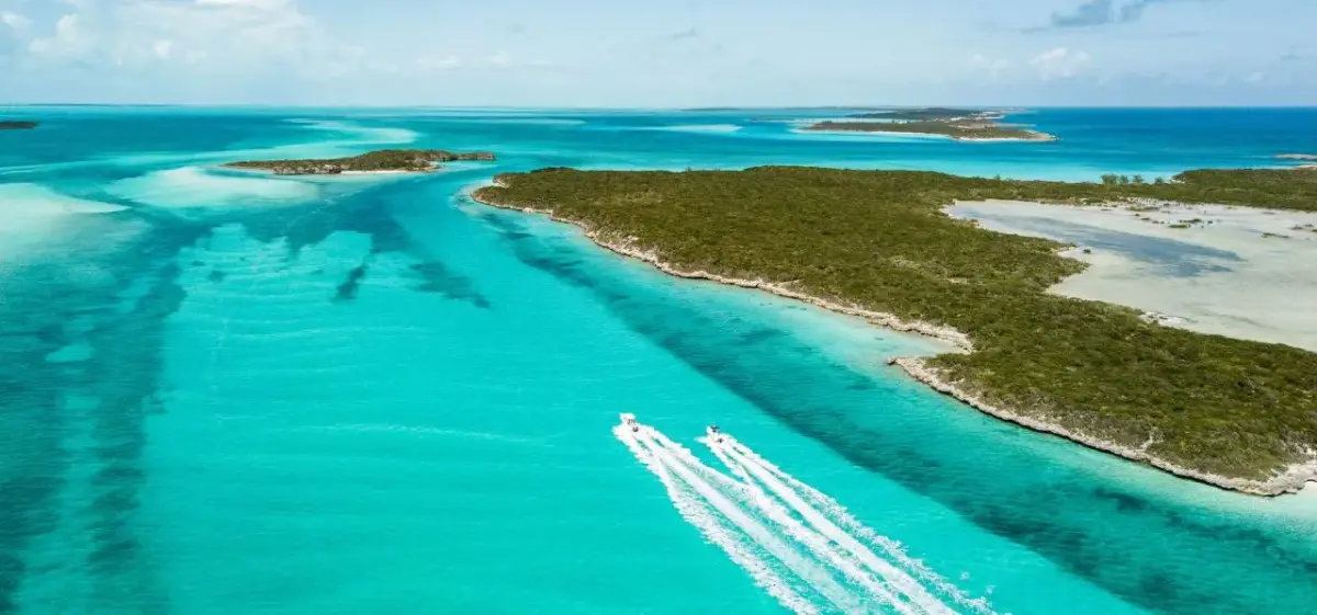 Aerial view of luxury yachts cruising through crystal-clear turquoise waters around pristine Exuma islands