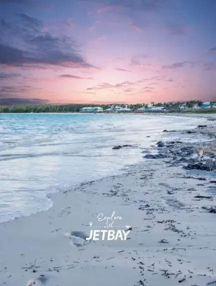 Pristine Exuma beach at sunset with pink sky, turquoise waters, and luxury beachfront homes in Bahamas