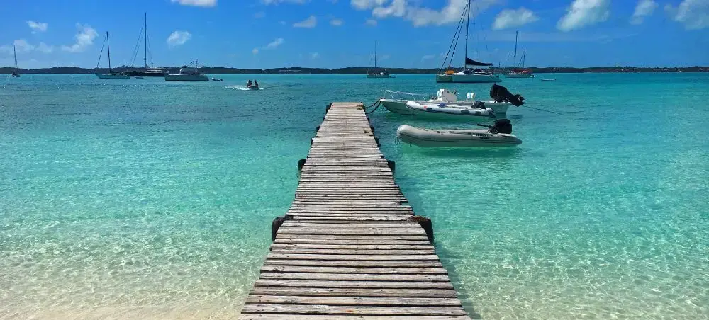 Wooden dock extending into crystal-clear turquoise waters with luxury yachts anchored in Exuma, Bahamas