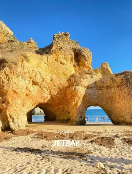 Golden limestone cliffs with natural arches frame turquoise waters at Faro's stunning Algarve coastline