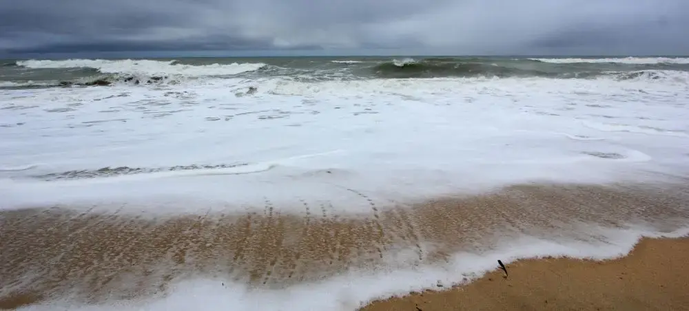 Dramatic ocean waves crash onto sandy Faro beach under stormy Portuguese skies, showcasing coastal beauty