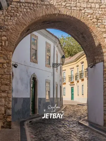 Historic stone archway framing cobblestone street and traditional Portuguese buildings in Faro's old town