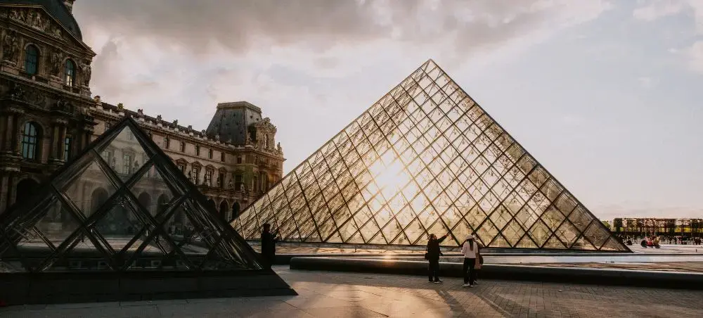 Louvre Museum's iconic glass pyramid and historic palace architecture at sunset in Paris, France