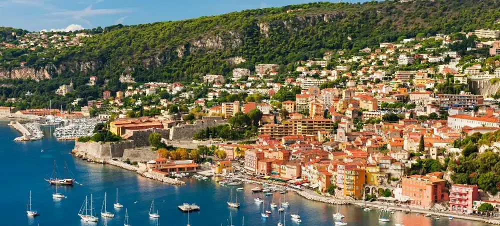 Scenic French Riviera coastal town with colorful buildings cascading down hillsides to azure harbor filled with luxury yachts