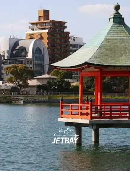 Traditional Japanese pagoda overlooking serene lake waters with modern Fukuoka cityscape in background