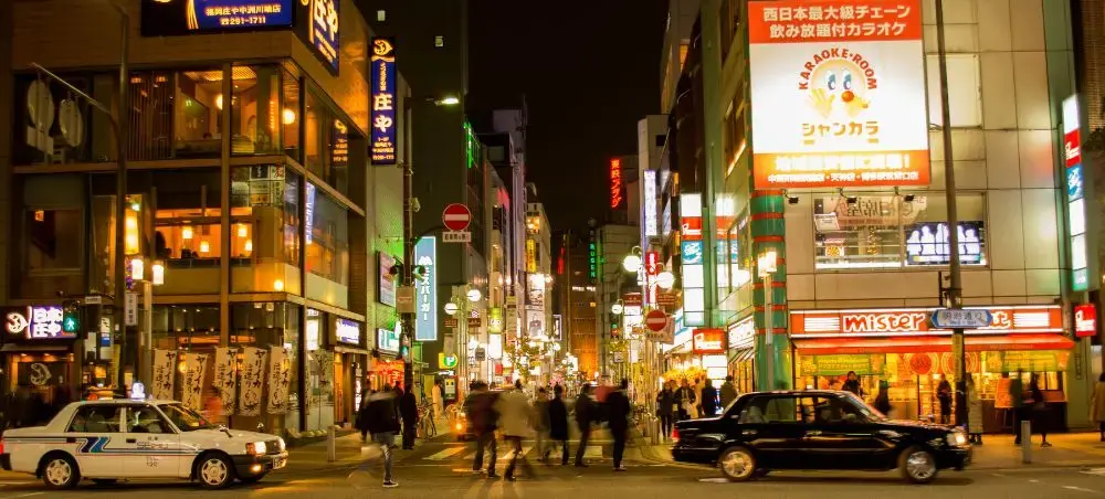 Bustling Fukuoka street at night with illuminated Japanese signs, restaurants, and pedestrians exploring the vibrant city