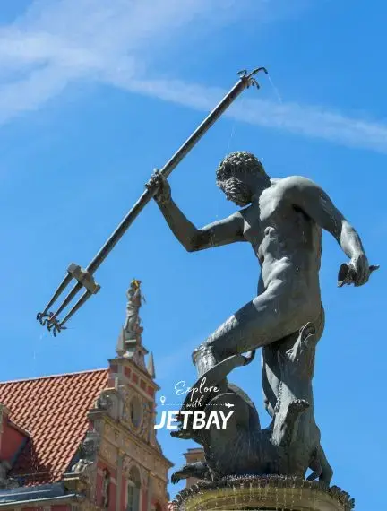 Neptune fountain statue with trident overlooking historic Gdansk architecture under bright blue sky