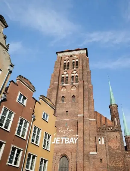 Historic St. Mary's Basilica tower dominates Gdansk's colorful Old Town architecture under blue skies