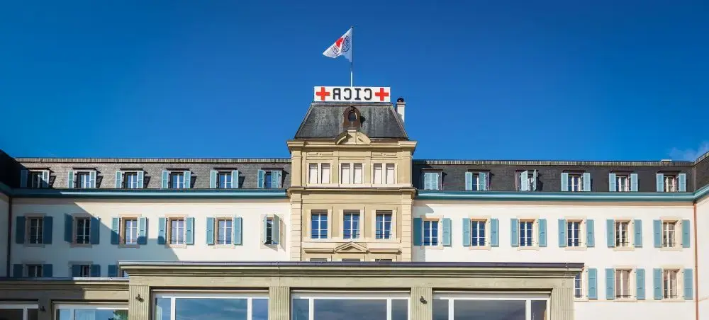 Historic Swiss hotel building with red cross signage and flag against clear blue sky in Geneva