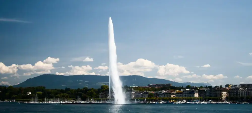 Geneva's iconic Jet d'Eau fountain shooting water high into Lake Geneva with Swiss Alps and cityscape
