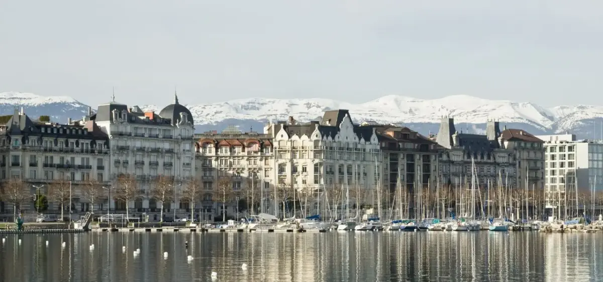Geneva waterfront with elegant Belle Époque buildings, marina filled with sailboats, and snow-capped Alps