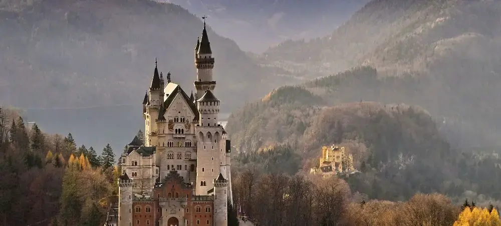 Neuschwanstein Castle rises majestically among autumn forests and Bavarian Alps, showcasing Germany's iconic architecture