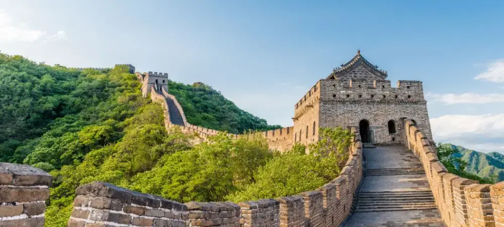 Great Wall of China winding through lush green mountains with ancient watchtowers under blue sky