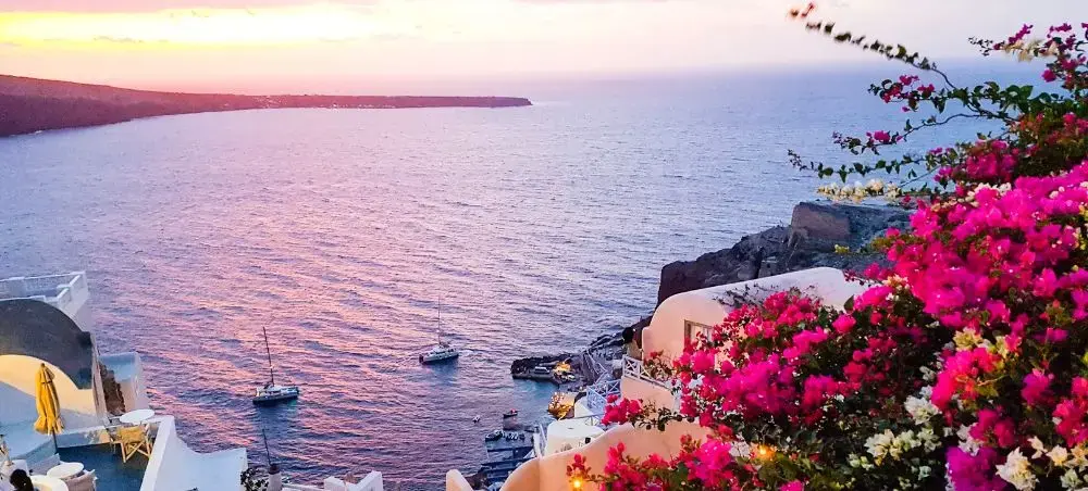 Stunning sunset view over Greek islands with vibrant bougainvillea flowers and luxury yachts in harbor