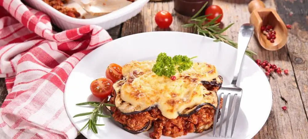 Authentic Greek moussaka with golden cheese topping, eggplant, and meat sauce on rustic wooden table