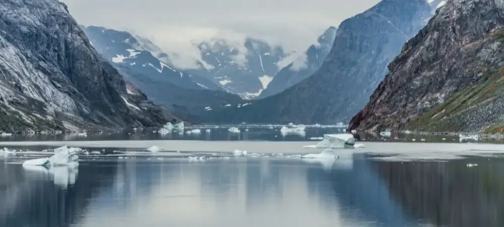 Pristine Arctic fjord in Greenland with floating icebergs surrounded by snow-capped mountains and calm waters