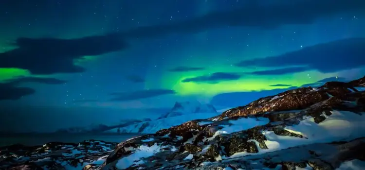 Spectacular northern lights dancing across starlit sky above snow-covered Greenland mountains and tundra