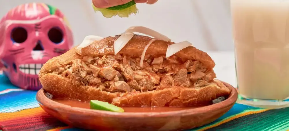 Traditional Mexican torta ahogada sandwich with spicy sauce served on colorful plate in Guadalajara