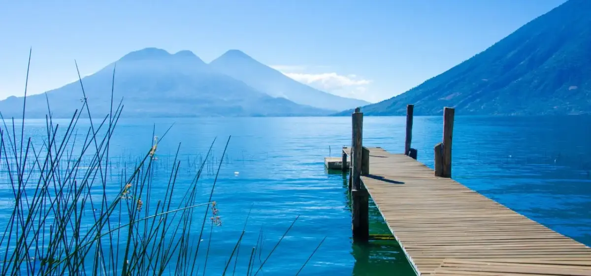 Serene wooden dock extending into pristine blue lake waters with volcanic mountains in Guatemala