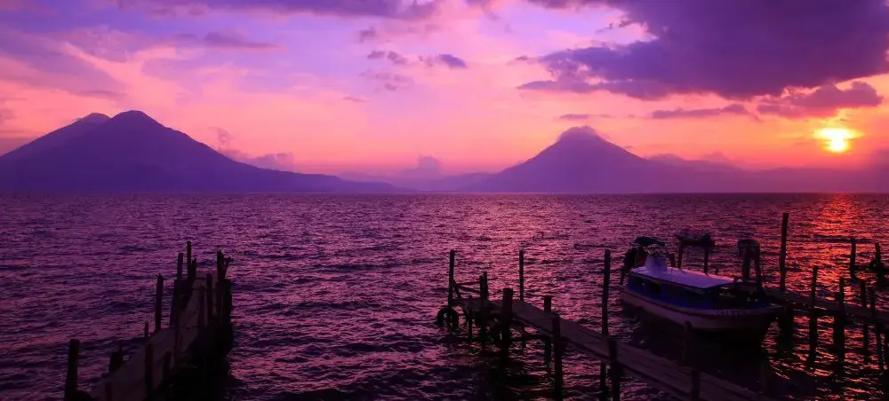 Stunning sunset over Lake Atitlán with volcanic peaks and traditional boats, showcasing Guatemala's natural beauty