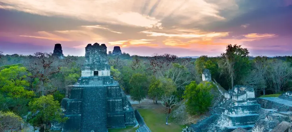 Ancient Mayan temples rise above lush jungle canopy at Tikal National Park during golden sunset in Guatemala