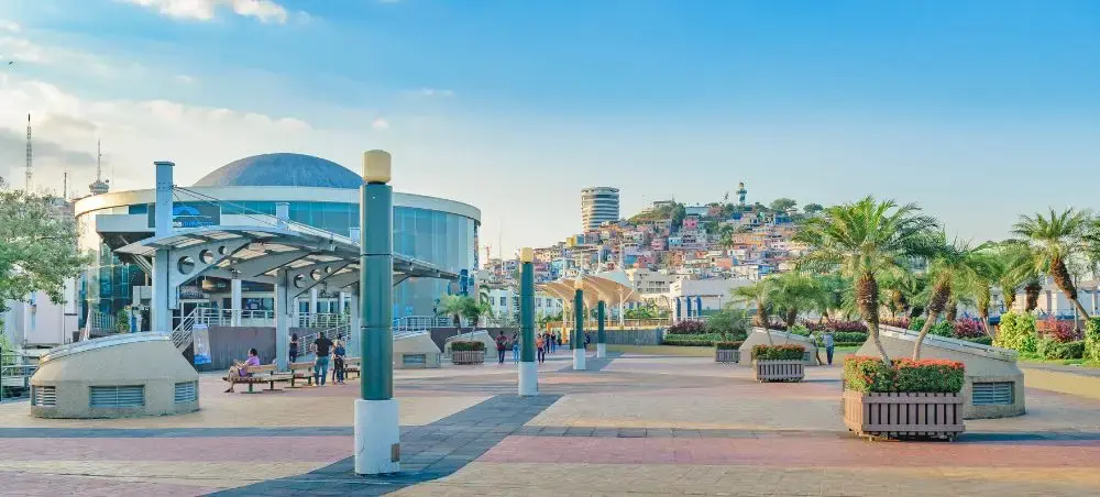 Modern waterfront promenade in Guayaquil with glass pavilion and hillside cityscape under blue sky