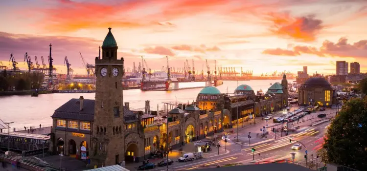 Hamburg's historic port district and iconic clock tower illuminated at sunset with bustling harbor cranes