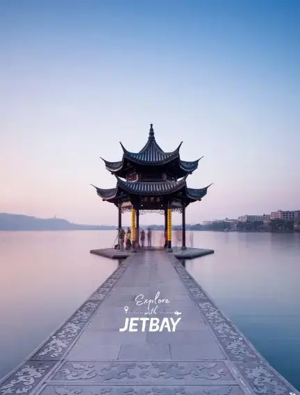 Traditional Chinese pagoda pavilion on stone walkway over West Lake at sunset in Hangzhou, China