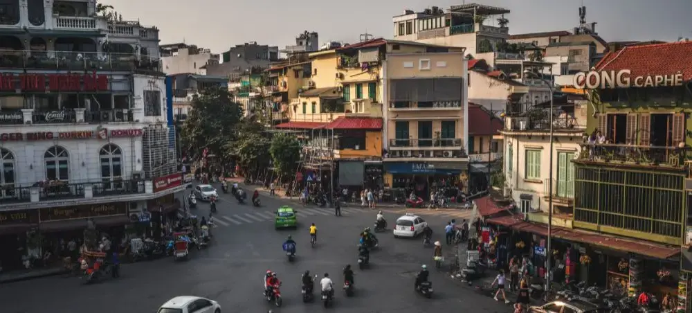 Bustling Hanoi street intersection with colorful colonial buildings, motorbikes, and pedestrians in Vietnam's capital